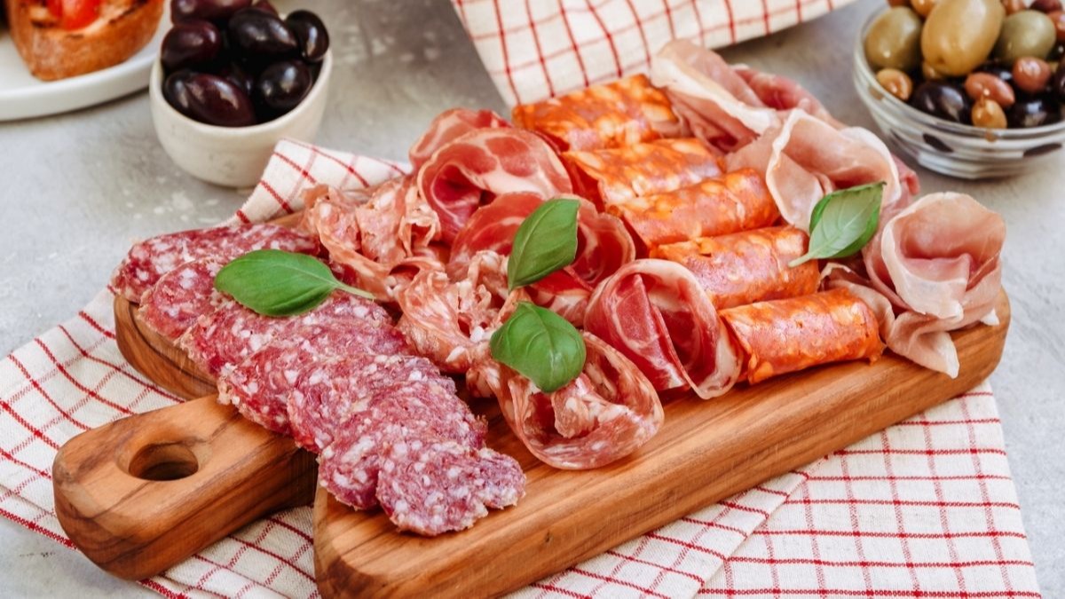 A charcuterie board with sliced salami, prosciutto, and chorizo, garnished with basil leaves.