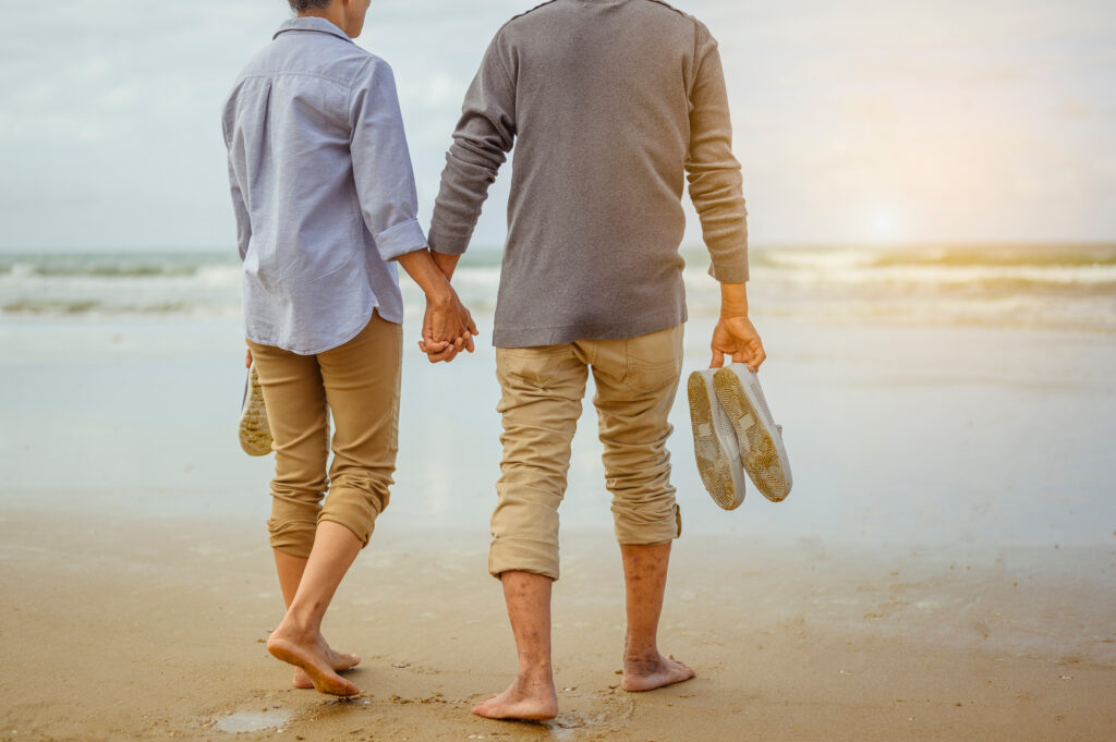 Senior couple walking on the beach holding hands at sunrise, plan life insurance at retirement concept.
