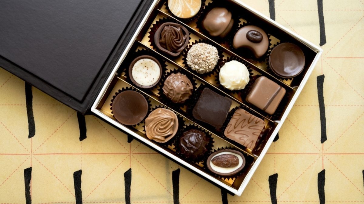 A box of assorted chocolates with various shapes and toppings on a patterned background.